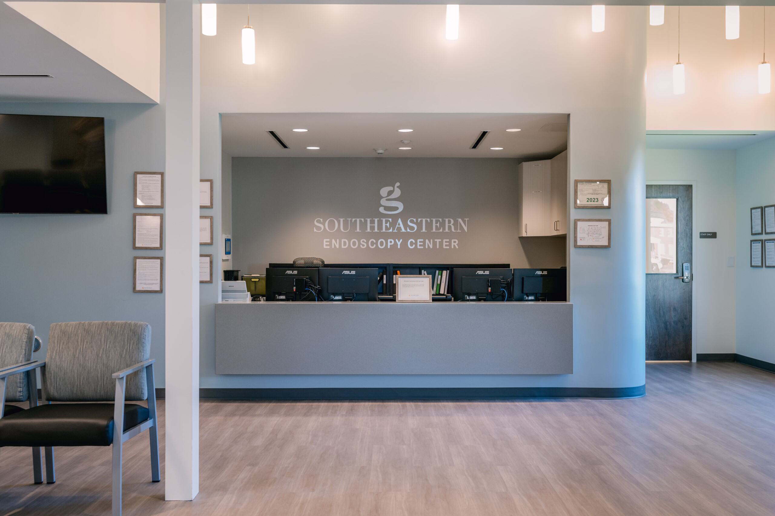 Reception area of Southeastern Endoscopy Center with modern desk, chairs, lights, plaques, a door right. Clean, neutral tones.